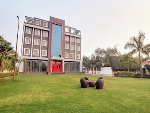 Un hotel con fachada moderna, entrada roja y césped cuidado con mobiliario exterior.