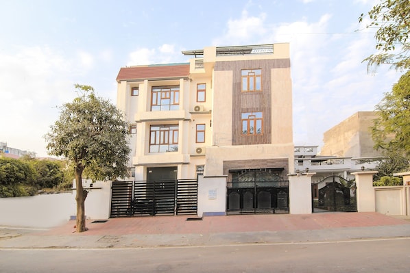 A multi-story residential building with a gated entrance, a tree in front, and a clear sky. - HOTEL O JMD INN (Lucknow)