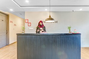 Una reception con una persona dietro al bancone, una parete con i numeri delle camere e un cartello che indica 'RECEPTION'.