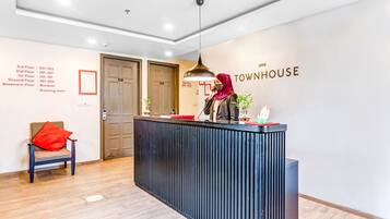 A hotel reception desk with a woman behind it, a sign for the 'Townhouse' hotel, and a list of room numbers on the wall.