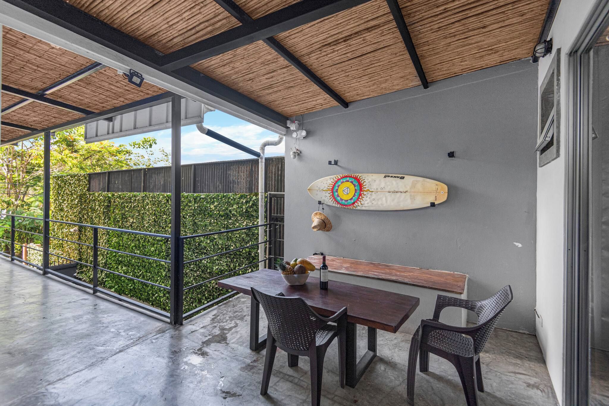 An outdoor patio with a table and chairs, a surfboard, and a bottle of wine.