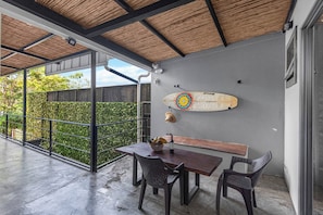 An outdoor patio with a table and chairs, a surfboard, and a bottle of wine. - Beachside Studio With Rooftop Views (Jacó)