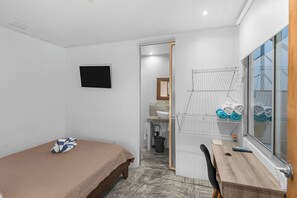 A compact room with a single bed, a desk, a window, and a wall-mounted TV. - Beachside Studio With Rooftop Views (Jacó)