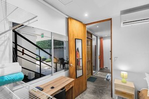A modern interior with a wooden door, a small table, a bench, and a bed with a headboard. - Beachside Studio With Rooftop Views (Jacó)