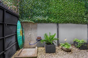 A small outdoor area with a concrete wall, a surfboard, a helmet, and several potted plants. - Beachside Studio With Rooftop Views (Jacó)
