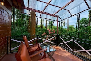Un espacio de estar al aire libre cubierto con sillas y una mesa de vidrio, rodeado de exuberante follaje y vistas al bosque.