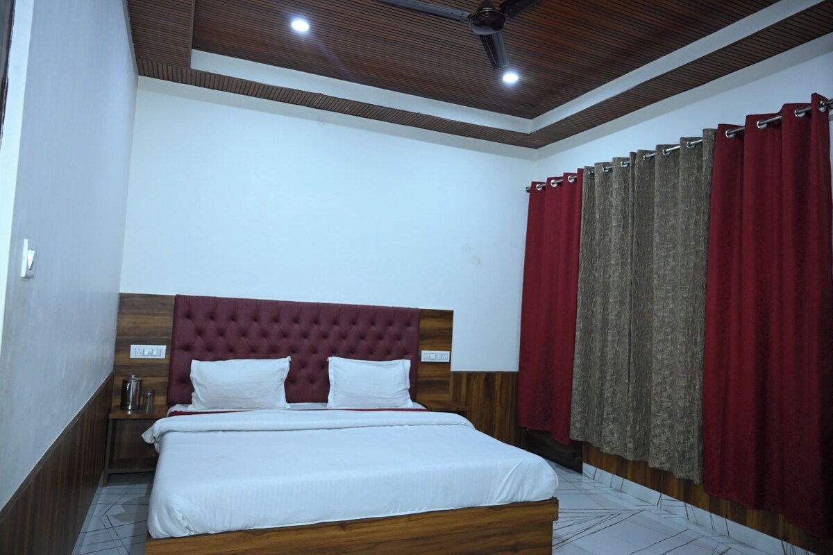 A bedroom with a wooden headboard, a bed with white bedding, a nightstand, and a red curtain.