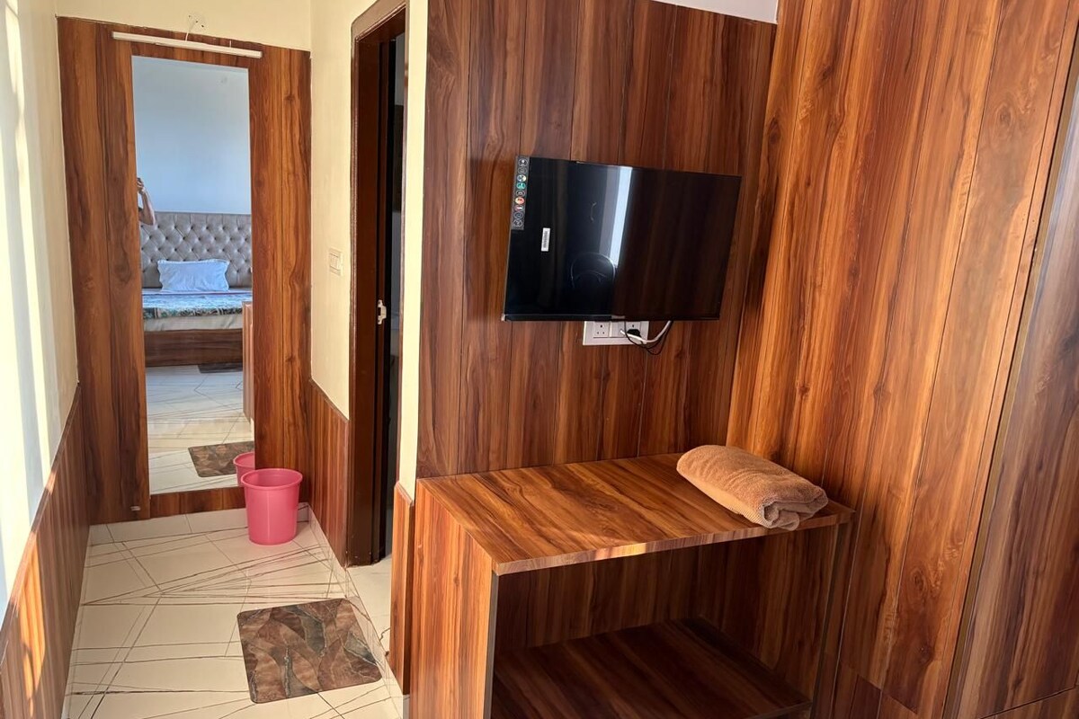 A room with a wooden wall panel, a flat-screen TV mounted above a wooden bench, and a pink bucket on the floor.