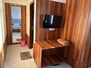 A room with a wooden wall panel, a flat-screen TV mounted above a wooden bench, and a pink bucket on the floor. - Shimla Eco Village (Shimla)