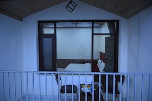 A balcony with a view of a room containing a bed, a chair, and a table with a fruit basket. - Shimla Eco Village (Shimla)