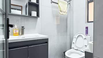 A modern bathroom with a toilet, a sink with a soap dispenser, a towel rack, and a mirror.