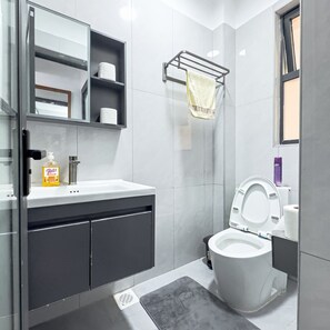 Een moderne badkamer met een toilet, een wastafel met zeepdispenser, een handdoekhouder en een spiegel.