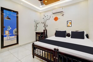 Quarto de hotel com cama grande, escrivaninha e uma cadeira. Há uma janela com vista para o céu e um quadro na parede.
