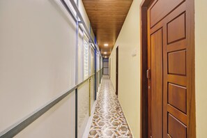 A hallway with patterned flooring, a wooden door, and a metal railing. - Hotel O PULARI BACKWATER & ROOMS (Neyyattinkara)