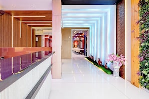 Un moderno vestíbulo de hotel con recepción, un largo pasillo y una pared decorativa con plantas.