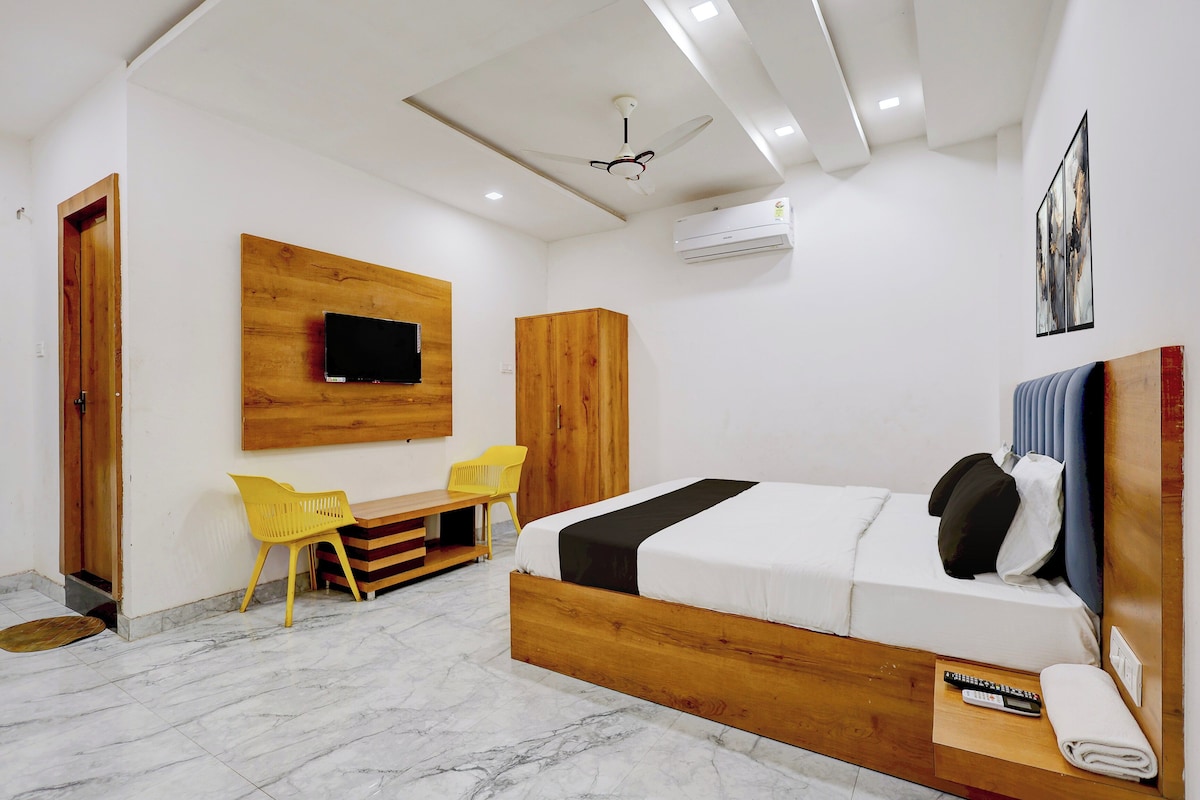 Habitación de hotel con cama, escritorio, dos sillas, televisor montado en la pared y ventilador de techo.