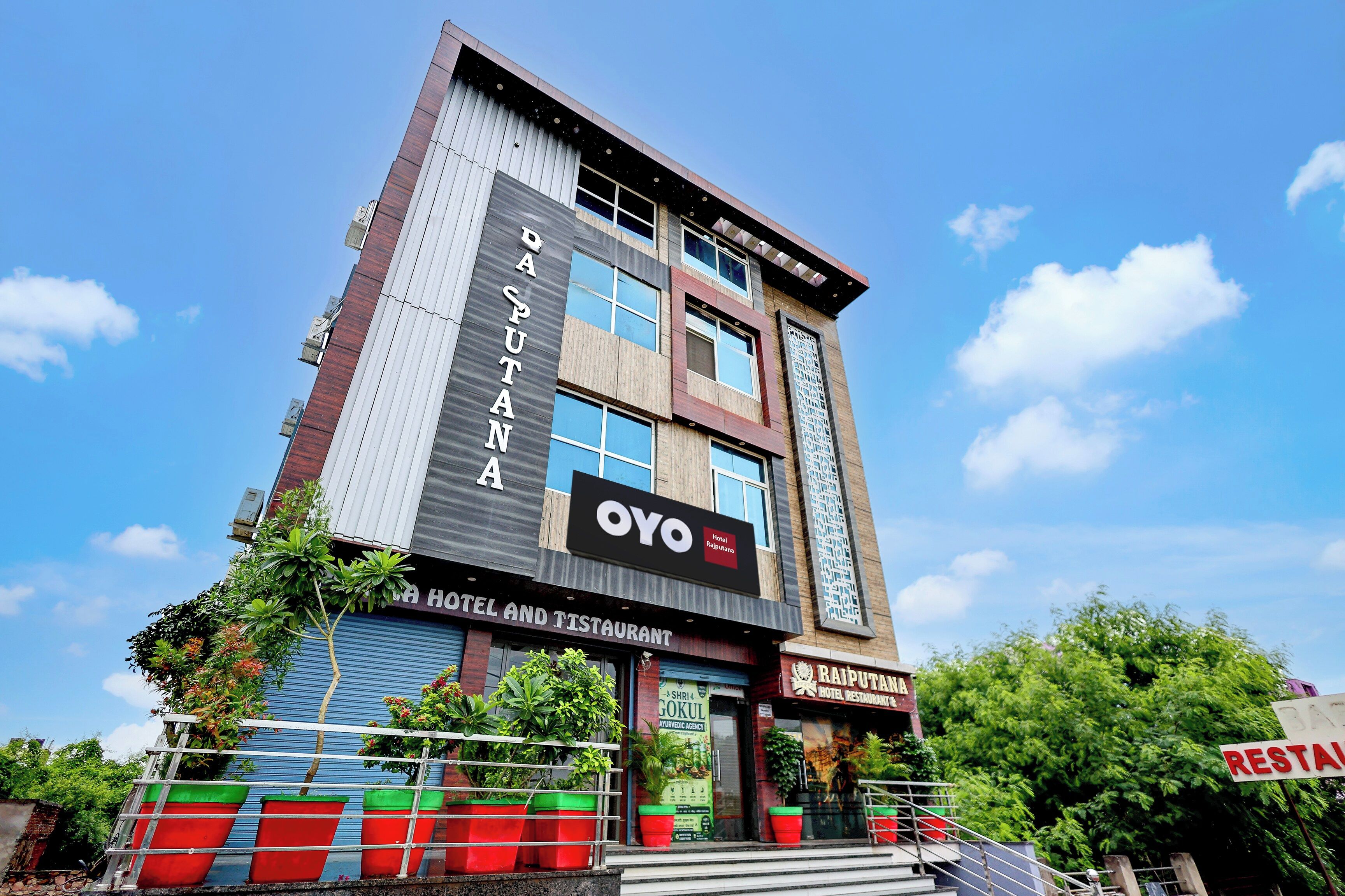 Un hotel de diverses plantes amb façana moderna, grans finestres i un cartell ben visible de 'OYO Hotel and Restaurant Rajputana'.