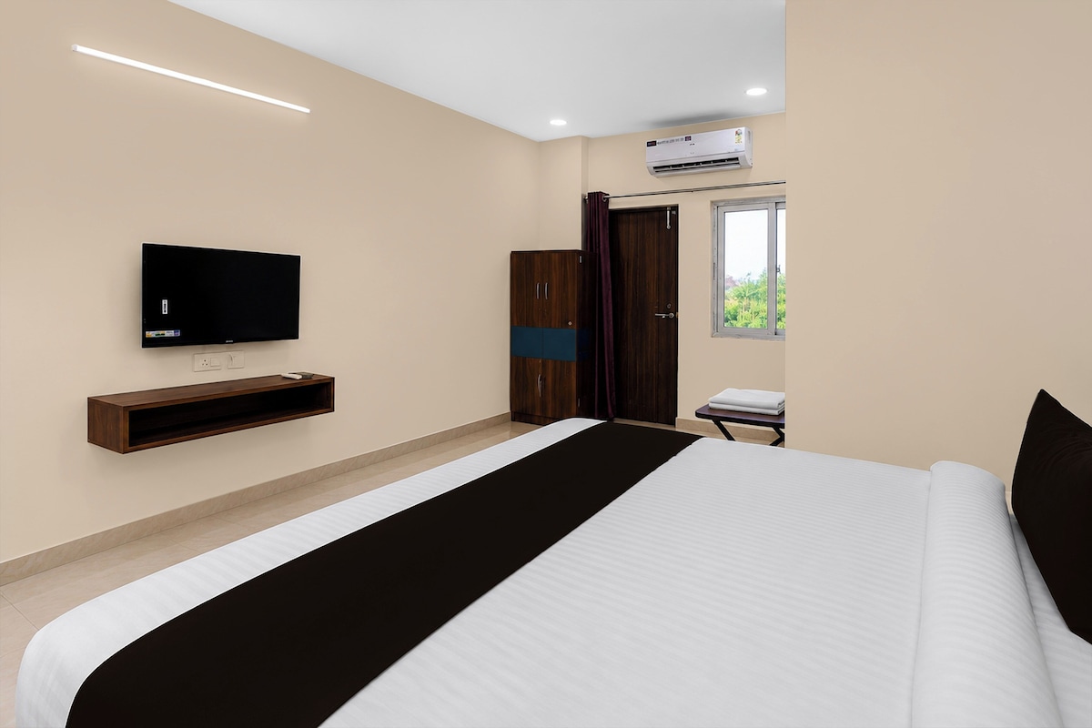 A modern hotel room with a large bed, a flat-screen TV mounted on the wall, a wardrobe, and an air conditioning unit.