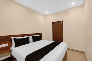 A bedroom with a wooden headboard, a bed with white and black bedding, a nightstand, and a door. - Hotel O Vaibhav Run Grand (Hyderabad)