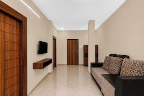 A hallway with a sofa, television, wooden doors, and a tiled floor. - Hotel O Vaibhav Run Grand (Hyderabad)