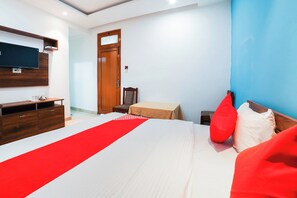 Una habitación de hotel con una cama, un armario de madera, un escritorio, una silla, un televisor montado en la pared y una puerta.