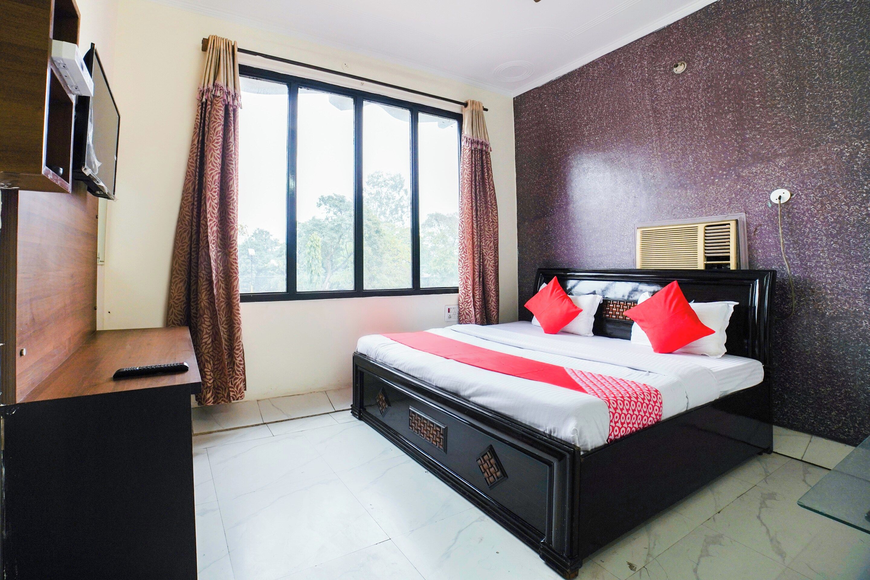 Habitación de hotel con cama, escritorio, televisión, ventana con cortinas y pared con textura.
