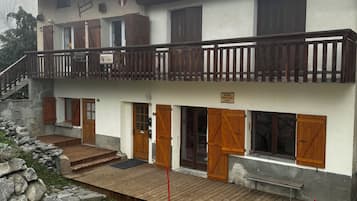 A two-story building with a balcony, wooden doors, and a stone wall.