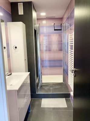 Ein modernes Badezimmer mit einem weißen Waschbecken, einer Duschkabine und einer Tür mit Griff.
