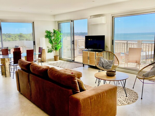 Ein modernes Wohnzimmer mit einer Couch, einem Fernseher und einem Balkon mit Meerblick.