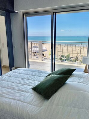 Ein Zimmer mit Bett, Blick auf den Strand und einem Balkon.
