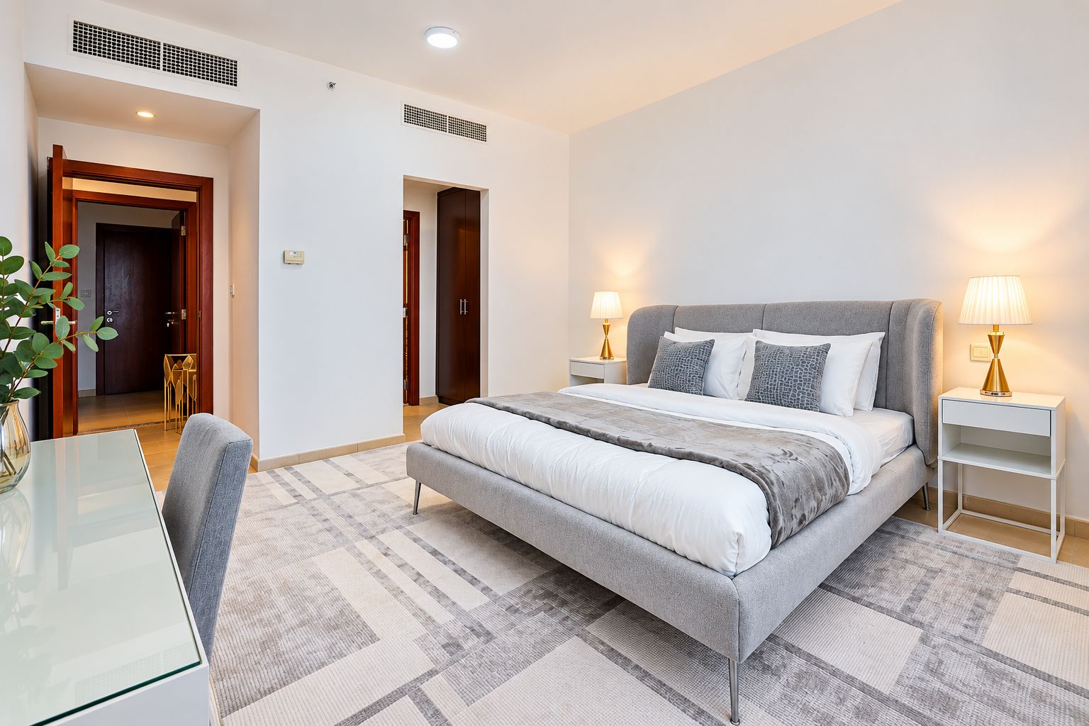 A modern bedroom with a large bed, bedside tables, a desk, and a chair.