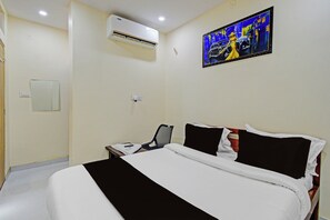 Habitació d'hotel amb llit, taulella de nit, aire condicionat fixat a la paret, quadre i presa elèctrica.