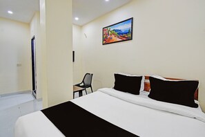 A hotel room with a bed, a chair, and a painting on the wall.
