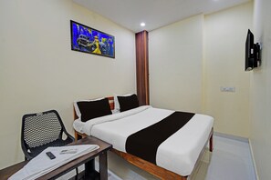A hotel room with a bed, a desk with a chair, a TV, and a painting on the wall.