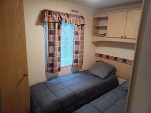 Ett litet sovrum med två sängar, ett fönster med gardiner och ett träskåp.