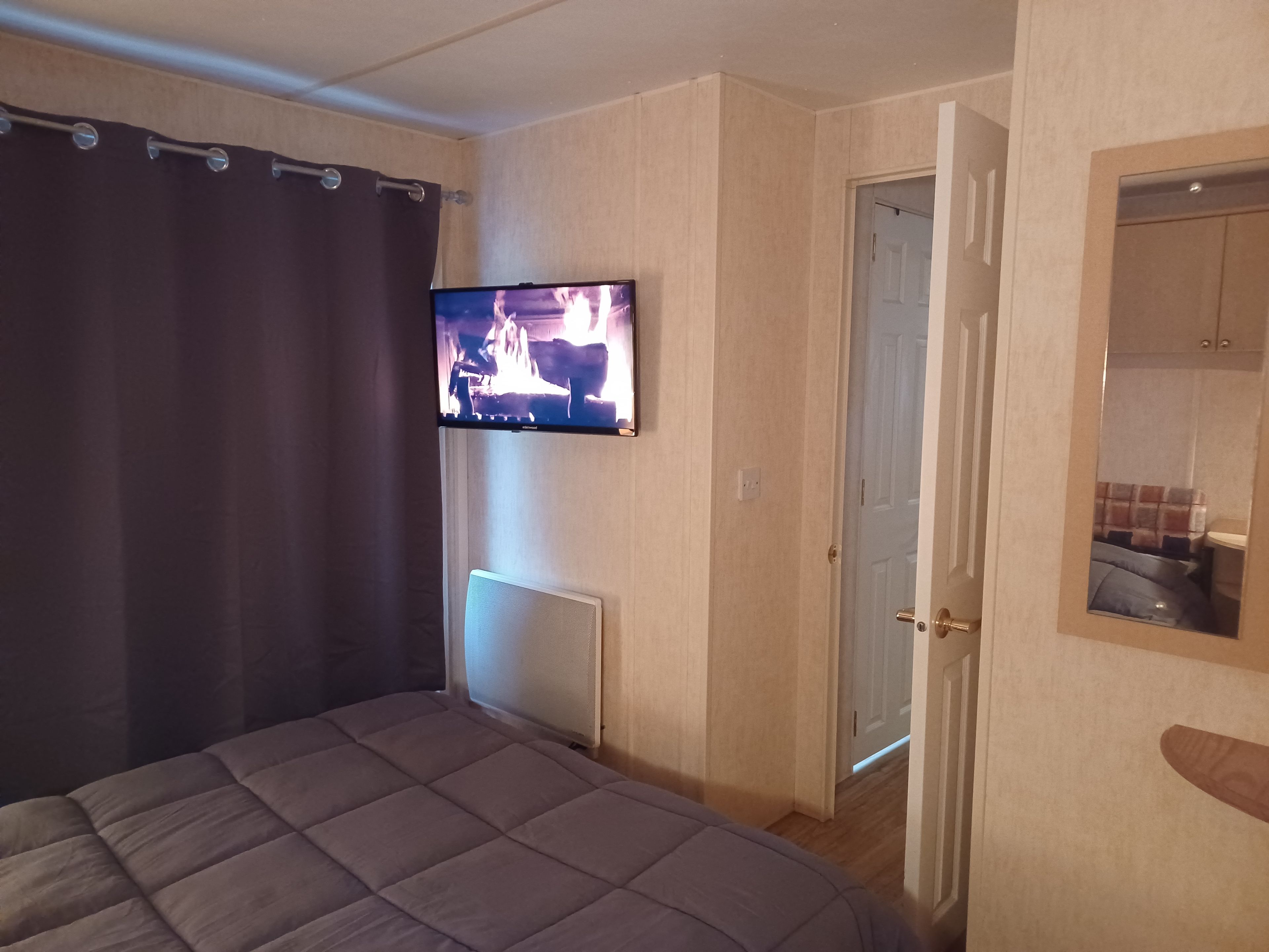 Een slaapkamer met een bed, een aan de muur bevestigde televisie, een deur en een spiegel.