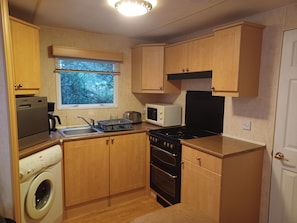 A compact kitchen with wooden cabinets, a washing machine, a microwave, and a stove. - New Listing (Peyrilhac)