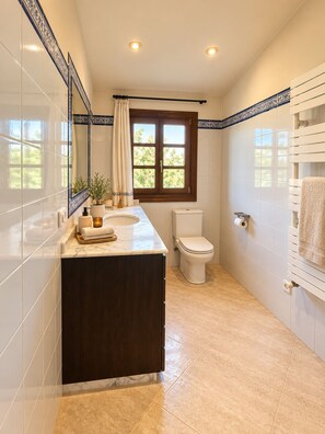 Ein Badezimmer mit Marmorwaschbecken, Toilette und einem Fenster mit Blick auf Grünflächen.
