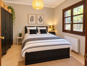 Ein Schlafzimmer mit einem Bett, Nachttischen, einem Heizkörper, einem Fenster und Wandbildern.