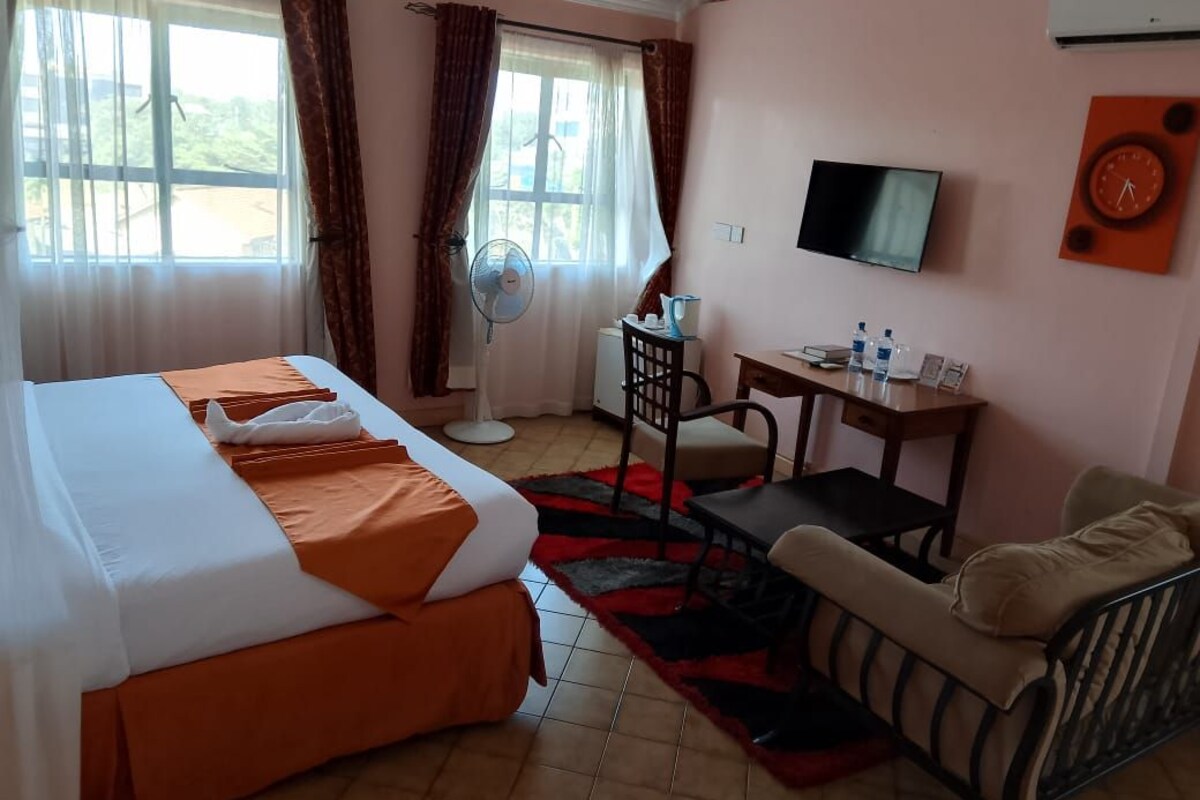 A hotel room with a bed, a desk, a chair, a television, and a window with curtains.