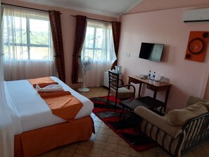 A hotel room with a bed, a desk, a chair, a television, and a window with curtains. - JUMUIA HOTEL KISUMU (Kisumu)