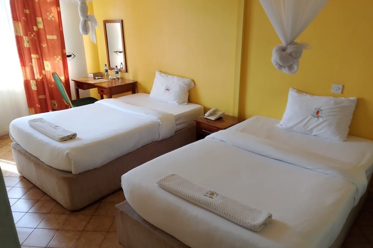 A hotel room with two beds, a desk, a chair, a mirror, and a curtain.
