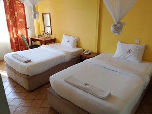 A hotel room with two beds, a desk, a chair, a mirror, and a curtain. - JUMUIA HOTEL KISUMU (Kisumu)