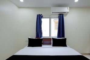 A hotel room with a bed, two pillows, a window with curtains, and an air conditioning unit. - Hotel O Sree Nirvi (Hyderabad)