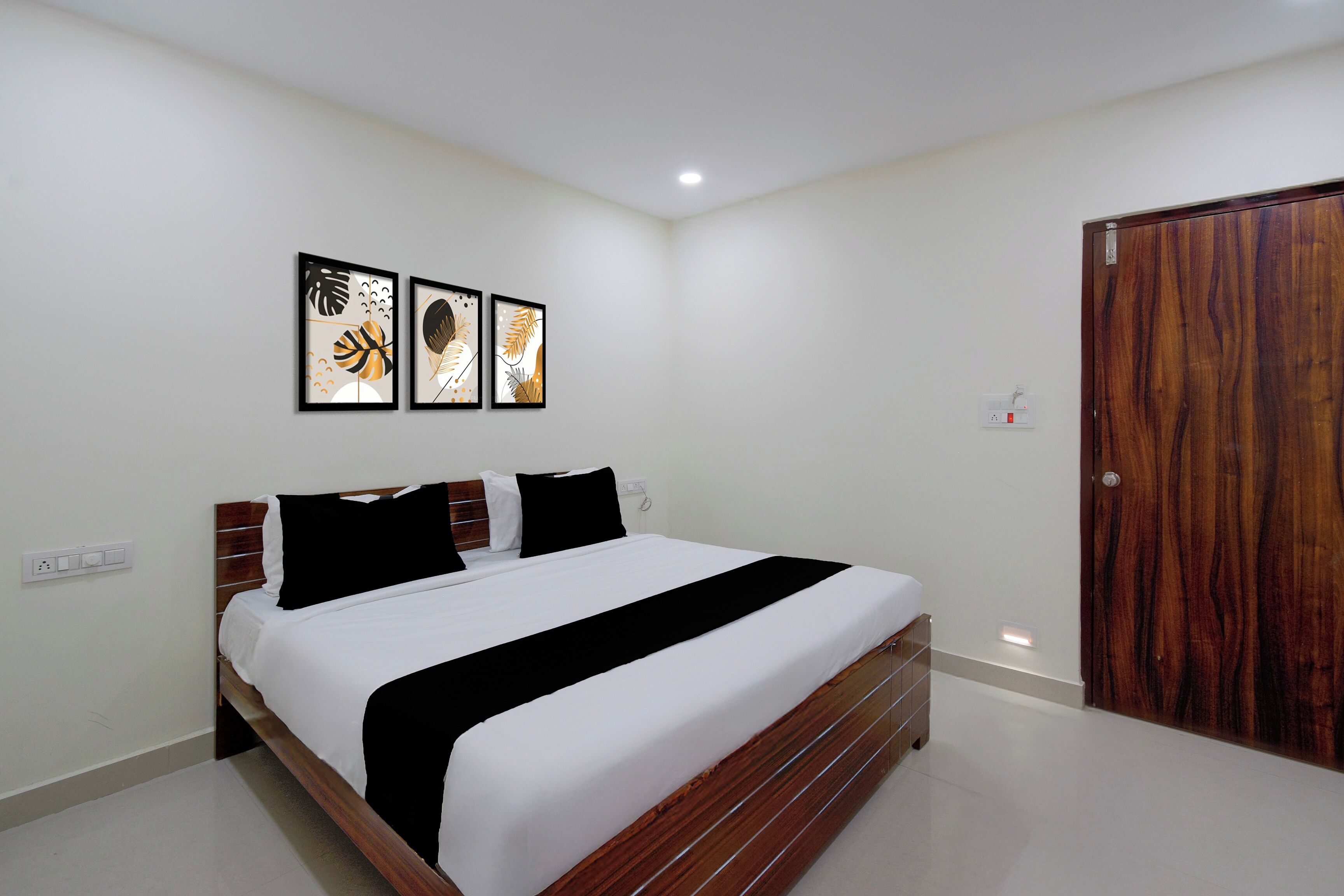 A bedroom with a bed, a wooden door, and three framed artworks on the wall.