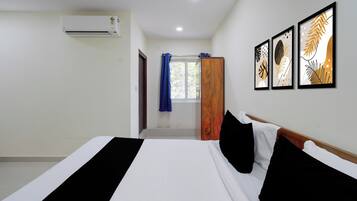 A hotel room with a bed, a window with curtains, an air conditioning unit, and framed artwork on the wall.