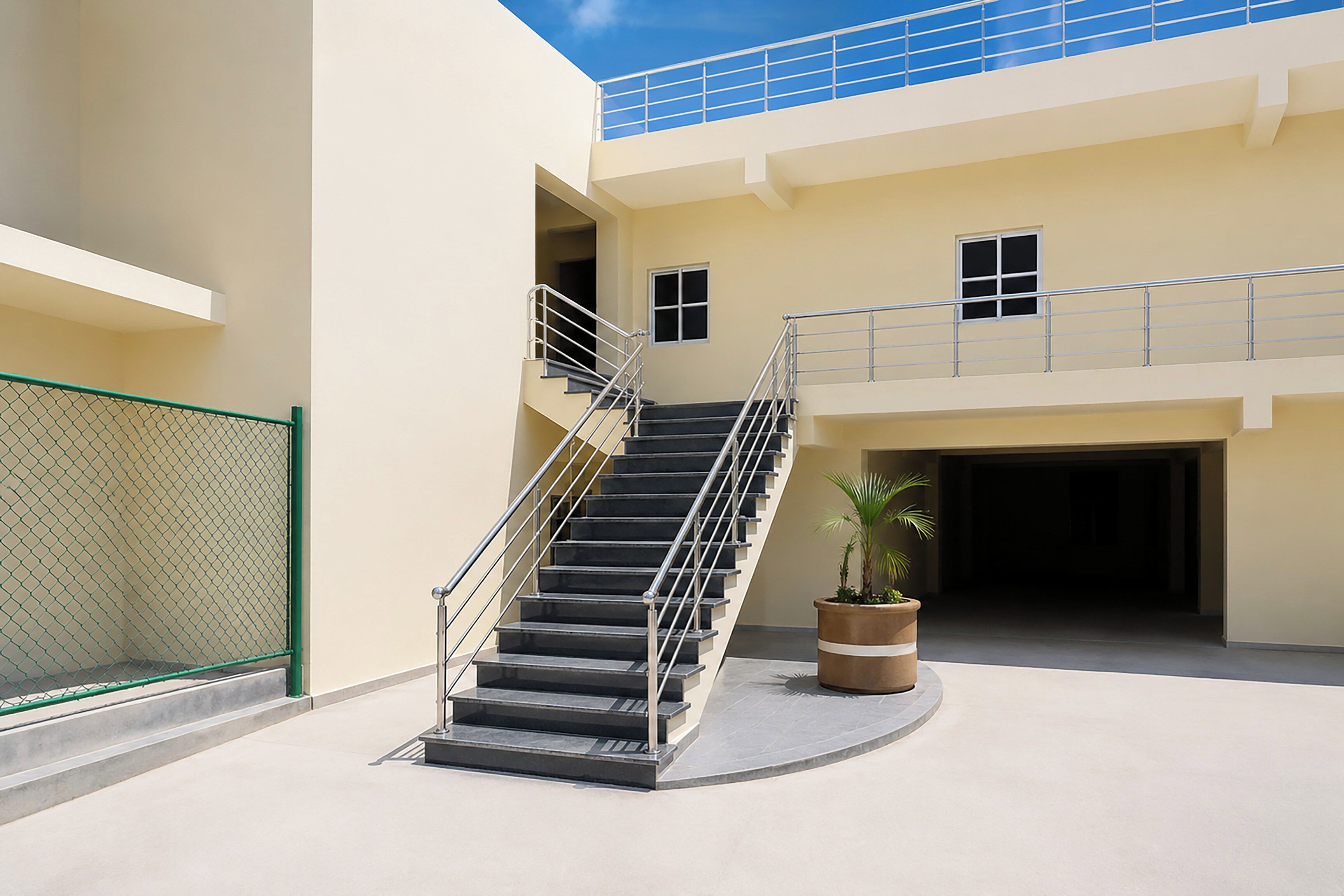 A multi-level building with a central staircase, a fenced area, and a potted plant.