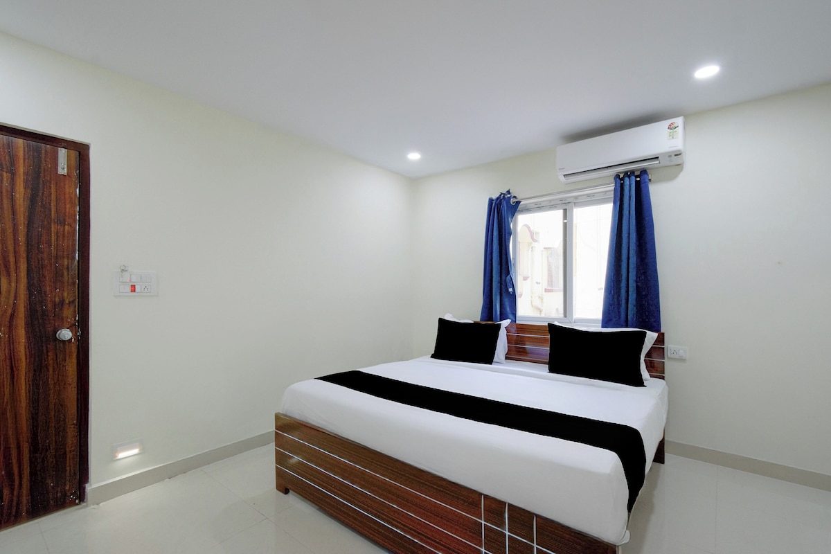 A bedroom with a wooden bed, white bedding, a window with blue curtains, and an air conditioning unit.