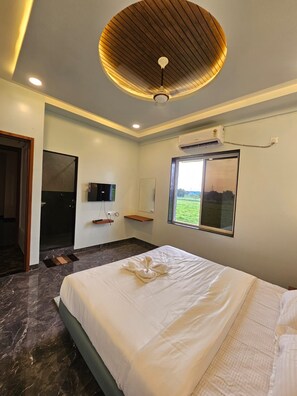 A hotel room with a bed, a ceiling fan, a mounted TV, and a window with a view of greenery. - SRG Hotel and Restruant (Borgaon)