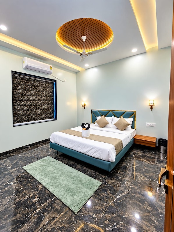 A hotel room with a bed, a ceiling fan, a wall-mounted air conditioner, a wall art piece, and a marble floor. - SRG Hotel and Restruant (Borgaon)